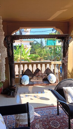 Ein Balkon mit einer Schaukel, einem gemusterten Teppich und Blick auf Grünflächen und Gebäude.