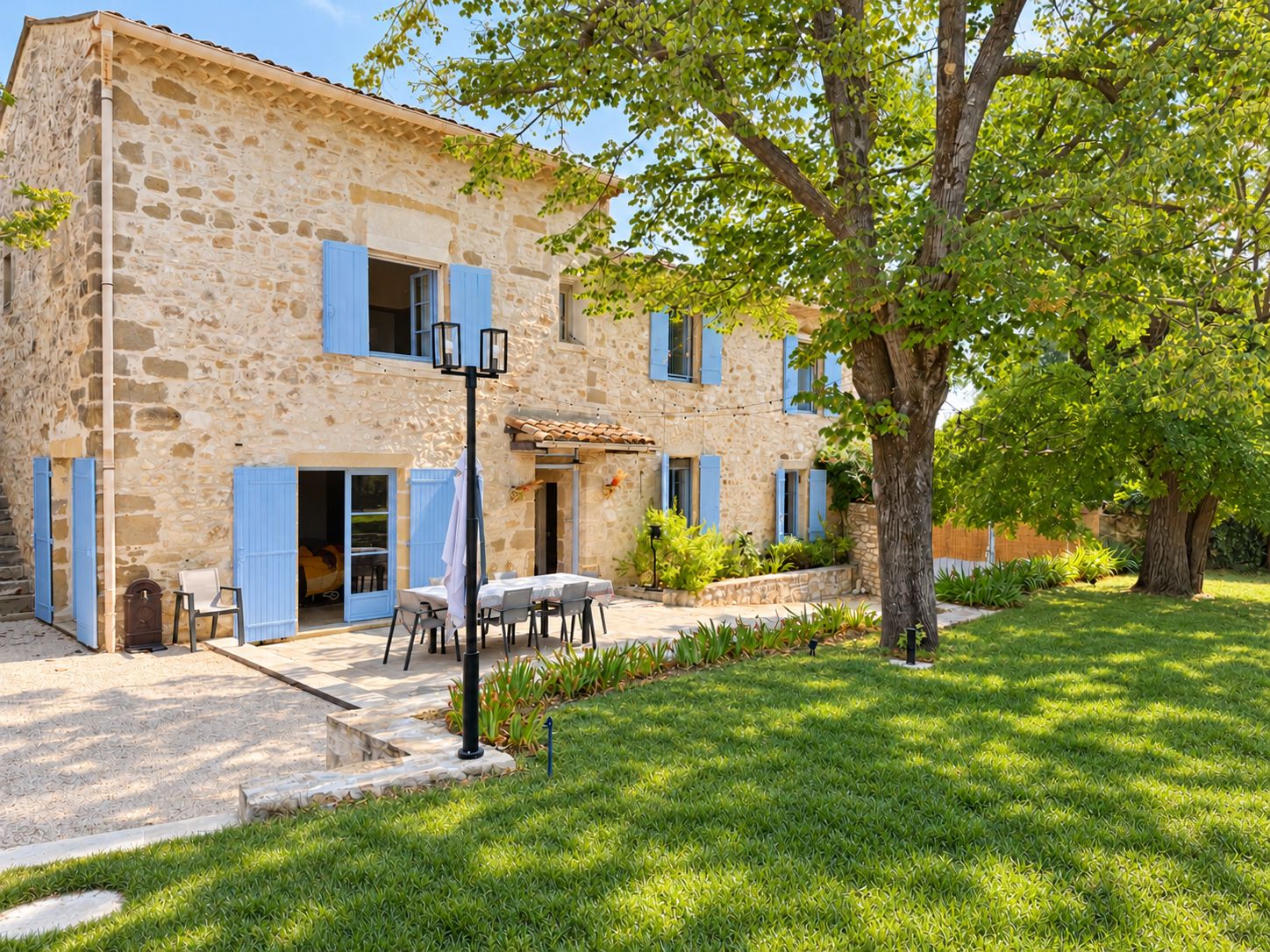 A stone building with blue shutters, a patio with outdoor seating, and a well-maintained lawn.