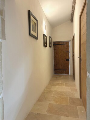 Ein Flur mit Steinfußboden, Holztüren und gerahmten Bildern an der Wand.