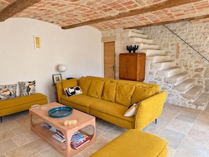 A living room with a yellow sofa, a wooden coffee table, and a stone wall with a staircase. - Authentic farmhouse with a pool, 10 minutes from Uzès, for 8 people (Garrigues-Sainte-Eulalie)