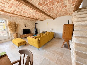A living room with a yellow sofa, a television, and a fireplace. - Authentic farmhouse with a pool, 10 minutes from Uzès, for 8 people (Garrigues-Sainte-Eulalie)