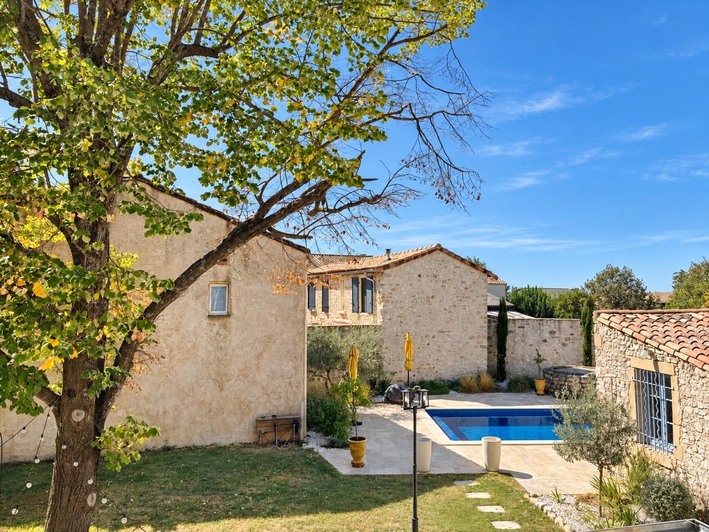A stone building with a swimming pool, surrounded by a well-maintained lawn and a tree.