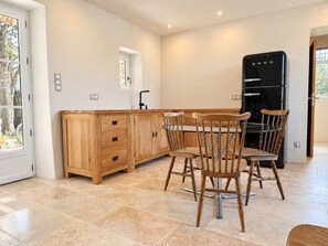 A modern kitchen with wooden cabinetry, a black refrigerator, and a dining table with chairs. - Authentic farmhouse with a pool, 10 minutes from Uzès, for 8 people (Garrigues-Sainte-Eulalie)