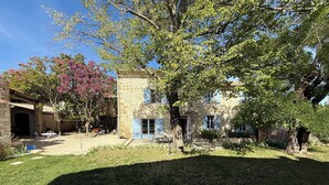 Un edificio in pietra con un patio, un albero con fiori rosa e un prato.
