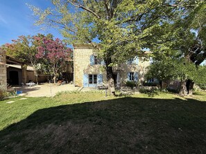 A stone building with a patio area, a tree with pink flowers, and a grassy yard. - Authentic farmhouse with a pool, 10 minutes from Uzès, for 8 people (Garrigues-Sainte-Eulalie)