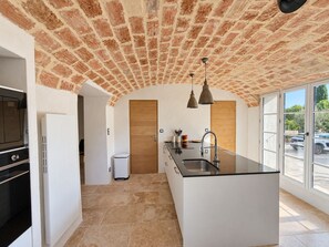 A kitchen with a brick ceiling, a central island with a sink, pendant lights, and a view of the outside. - Authentic farmhouse with a pool, 10 minutes from Uzès, for 8 people (Garrigues-Sainte-Eulalie)