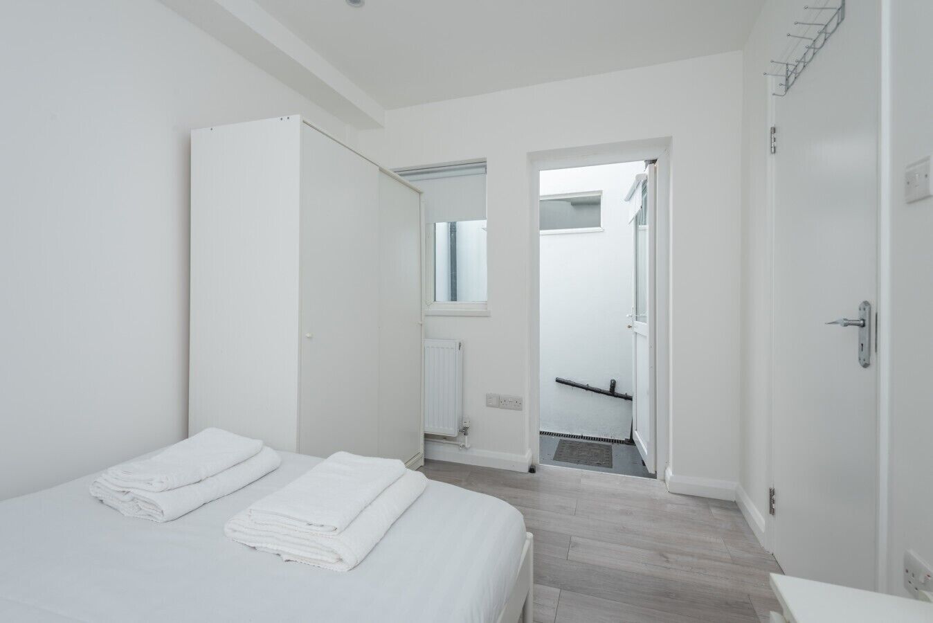 A minimalist hotel room with a bed, a wardrobe, and a bathroom visible through an open door.