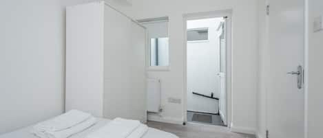 A minimalist hotel room with a bed, a wardrobe, and a bathroom visible through an open door.