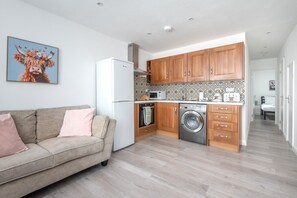 A compact kitchen with wooden cabinets, a washing machine, and a refrigerator. - Hackney Central | London Fields & Broadway Market (London)