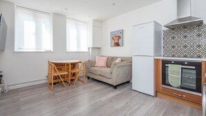 Eine moderne Küche mit Einbauofen, ein Essbereich mit Holztisch und -stühlen sowie eine Wohnbereich mit Sofa und Wanddeko.