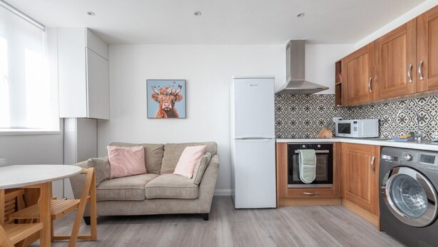 Eine kleine Küche mit Sofa, Waschmaschine, Mikrowelle und Kühlschrank.