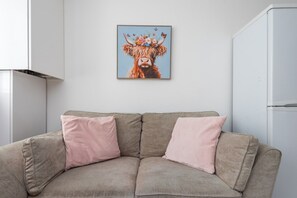 A beige sofa with pink cushions and a framed picture of a decorated animal on the wall. - Hackney Central | London Fields & Broadway Market (London)