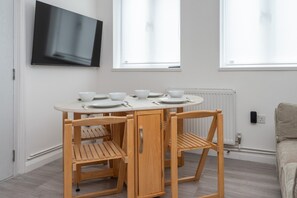 A dining area with a table set for four, a television mounted on the wall, and a window providing natural light. - Hackney Central | London Fields & Broadway Market (London)