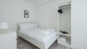 Ein schlicht eingerichtetes Schlafzimmer mit Bett, Nachttisch, Kleiderschrank und einem gerahmten Bild an der Wand.