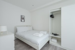 Ein schlicht eingerichtetes Schlafzimmer mit Bett, Nachttisch, Kleiderschrank und einem gerahmten Bild an der Wand.