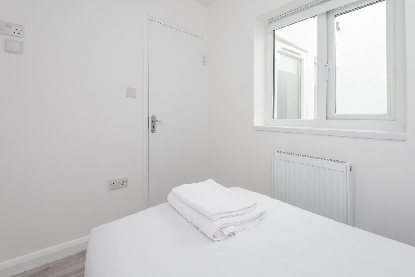 A white room with a bed, a window, and a radiator.