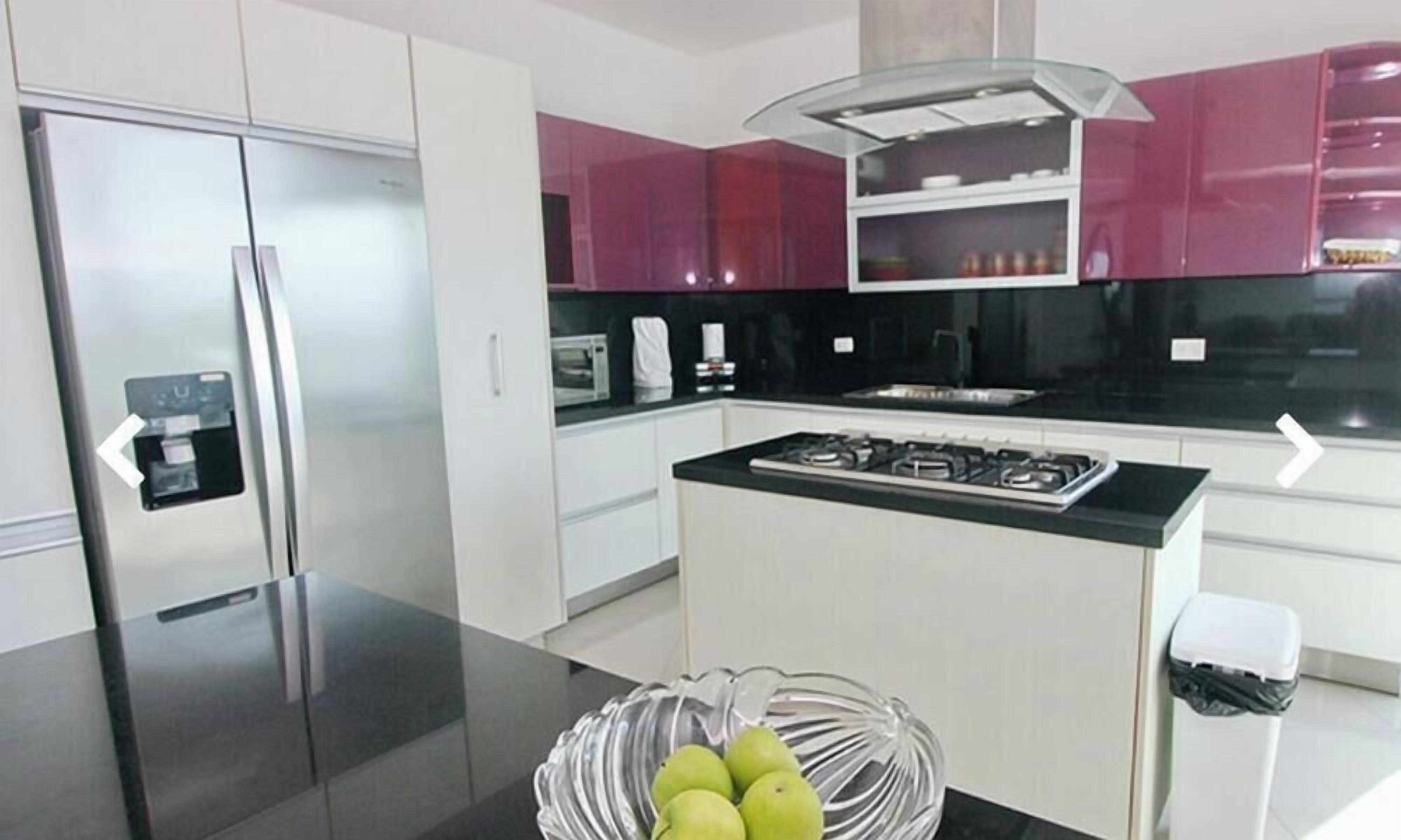 A modern kitchen with stainless steel appliances, a black countertop, and a bowl of green apples.