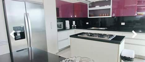A modern kitchen with stainless steel appliances, a black countertop, and a bowl of green apples.