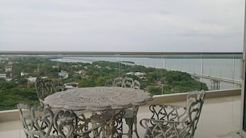 Un balcón con una mesa redonda y sillas de metal decorativas, con vista a un puente y una masa de agua.