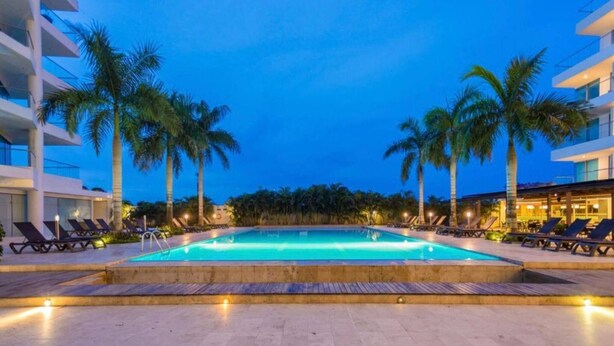Una piscina con lettini e palme, circondata da edifici.