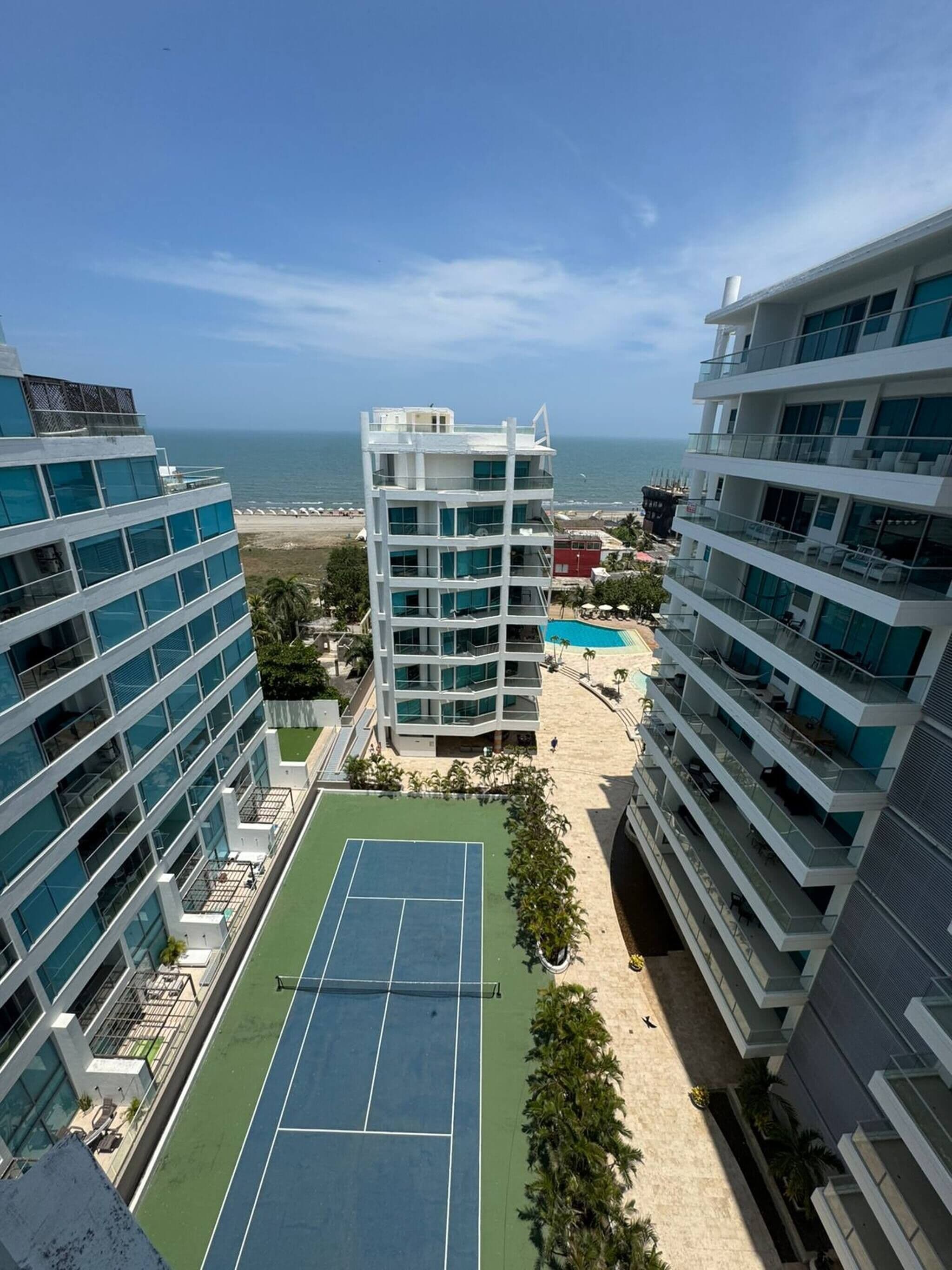Un hotel de varios pisos con cancha de tenis, piscina y vista al océano.