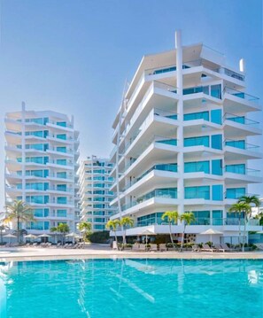 Un hotel moderno con varios balcones, piscina y palmeras.