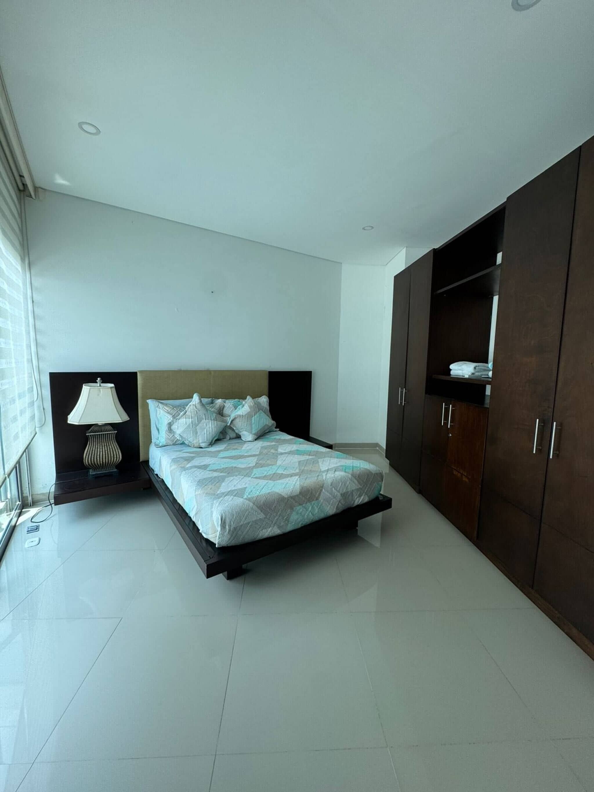 Un dormitorio con cama, mesita de noche, lámpara y armario.