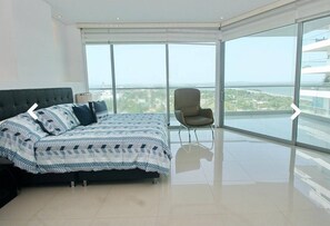 Ein modernes Schlafzimmer mit einem großen Bett, einem Sessel und einem Balkon mit Blick auf die Stadt.