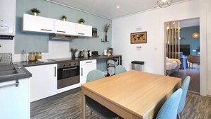 A modern kitchen with white cabinets, a wooden dining table, and blue chairs. - At the Bretzel Doré - Historic District (Colmar)