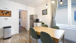 A dining area with a wooden table, four chairs, a refrigerator, a microwave, and a small plant. - At the Bretzel Doré - Historic District (Colmar)