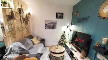 Kodikas olohuone, jossa on sohva, pieni pyöreä pöytä, televisio ja joulukuusi.