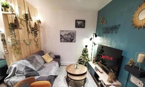 A cozy living room with a sofa, a small round table, a television, and a Christmas tree. - At the Bretzel Doré - Historic District (Colmar)