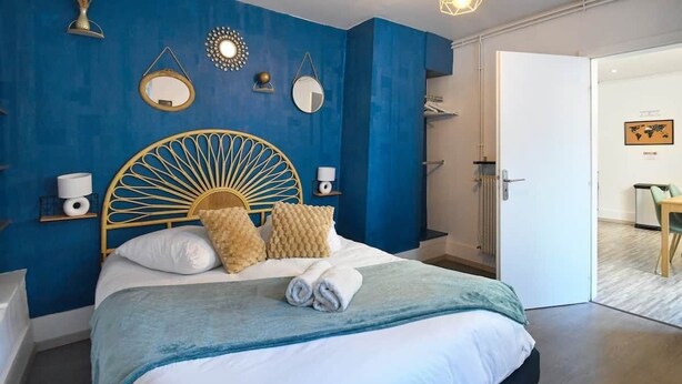 A bedroom with a bed, a round headboard, bedside tables, and a door leading to a bathroom. - At the Bretzel Doré - Historic District (Colmar)