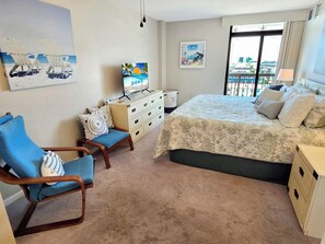 A hotel room with a bed, a desk, a chair, a television, and artwork on the walls. - Oceanfront 2 Bed 2 Bath Condo with Pool! Braemar Towers 1804 (Ocean City)