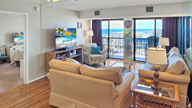 Una sala de estar con sofá, sillones, televisor y un balcón con vistas.
