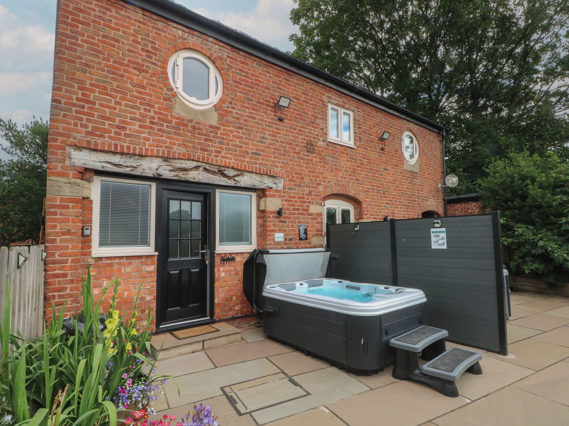 A brick house with a black door, two windows, a hot tub, and a covered patio area.