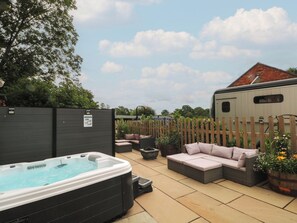 Ein Garten mit Whirlpool, Sitzgelegenheit im Freien, Holzzaun und einem Anhänger.
