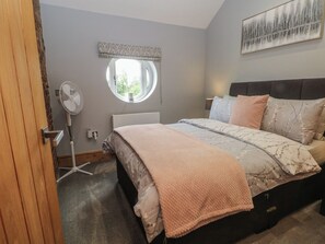 Ein Schlafzimmer mit einem Bett, einem runden Fenster, einem Standventilator und einem Bild an der Wand.