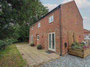 A brick house with a paved driveway, a wooden planter with flowers, and a garden area. - Barn 1 (Sandbach)