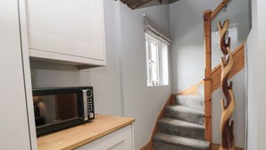 A compact kitchen with a microwave, a wooden staircase, and a window with blinds. - Barn 2 (Sandbach)