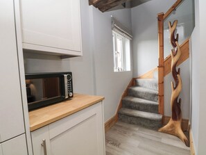 Eine kleine Küche mit Mikrowelle, einer Holztreppe und einem Fenster mit Jalousien.