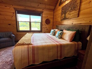 Ein Schlafzimmer einer Holzhütte mit einem Bett, einem Fenster, einer Couch und einer Baummalerei.