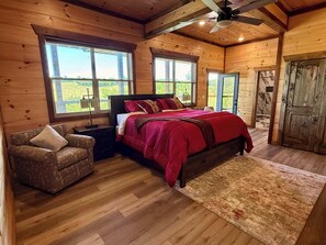 Ein Schlafzimmer einer Holzhütte mit einem Bett, einem Sessel und großen Fenstern.