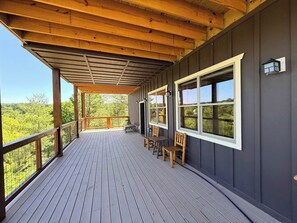 A covered deck with a wooden railing, a table and chairs, and large windows offering a view of the surrounding trees. - Lake Retreat Near Douglas Lake ,  Community Pool (Sevierville)