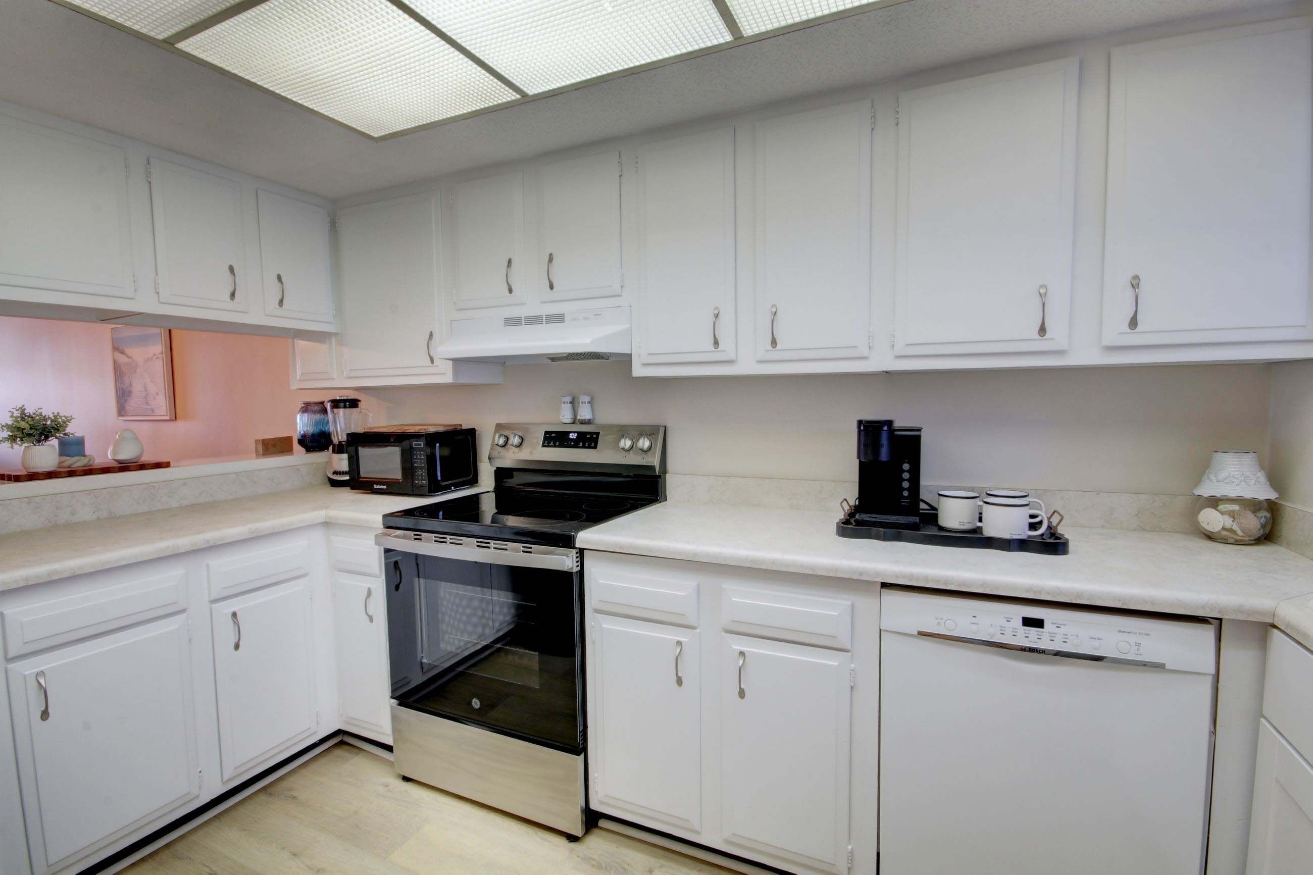 A modern kitchen with white cabinetry, a built-in oven, microwave, and coffee maker.