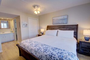 Ein Schlafzimmer mit Bett, Nachttischen, Spiegel, Tür und einem Wandbild.