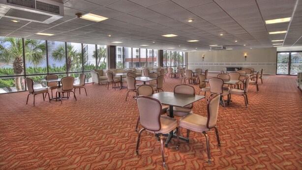 A large conference room with multiple tables and chairs, large windows with a view of palm trees, and a carpeted floor. - 151 El Matador 2 Bedroom Condo (Fort Walton Beach)