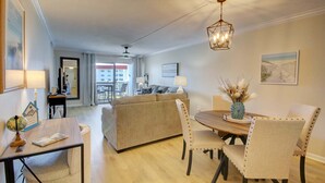 A modern living room with a dining area, a large window, and a view of the outside. - 151 El Matador 2 Bedroom Condo (Fort Walton Beach)