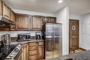 A kitchen with wooden cabinets, a stainless steel refrigerator, a microwave, and a coffee maker. - Premium Arrowhead Village 1br Condo Walk To Lift! 1 Bedroom Condo (Edwards)