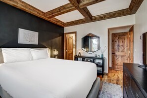 A bedroom with a large bed, a wooden ceiling, a dark wall, a mirror, and a wooden door. - Premium Arrowhead Village 1br Condo Walk To Lift! 1 Bedroom Condo (Edwards)